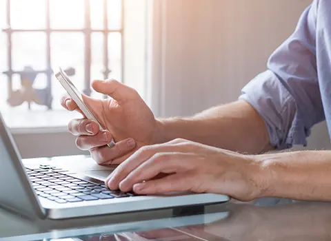 Junger Mann mit einer Hand am Laptop und der anderen am Smartphone