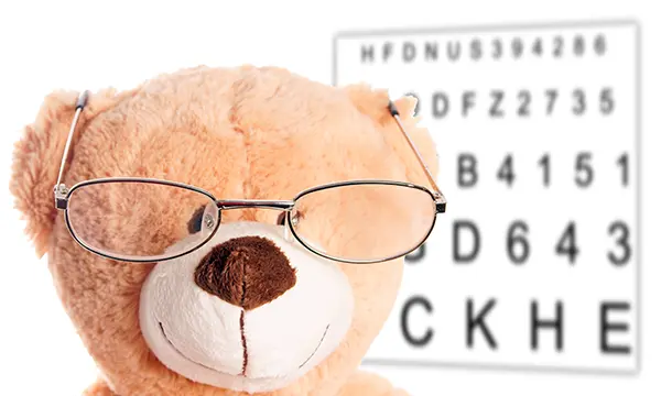 Teddybär mit Brille vor Buchstabentafel